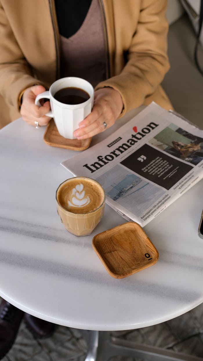 Person enjoying coffee while reading a newspaper in a cozy café setting.